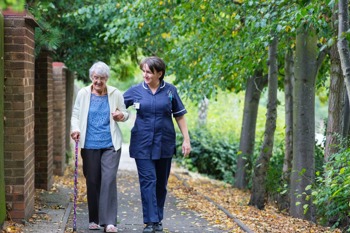 nurse and elderly lady walking on sidewalk