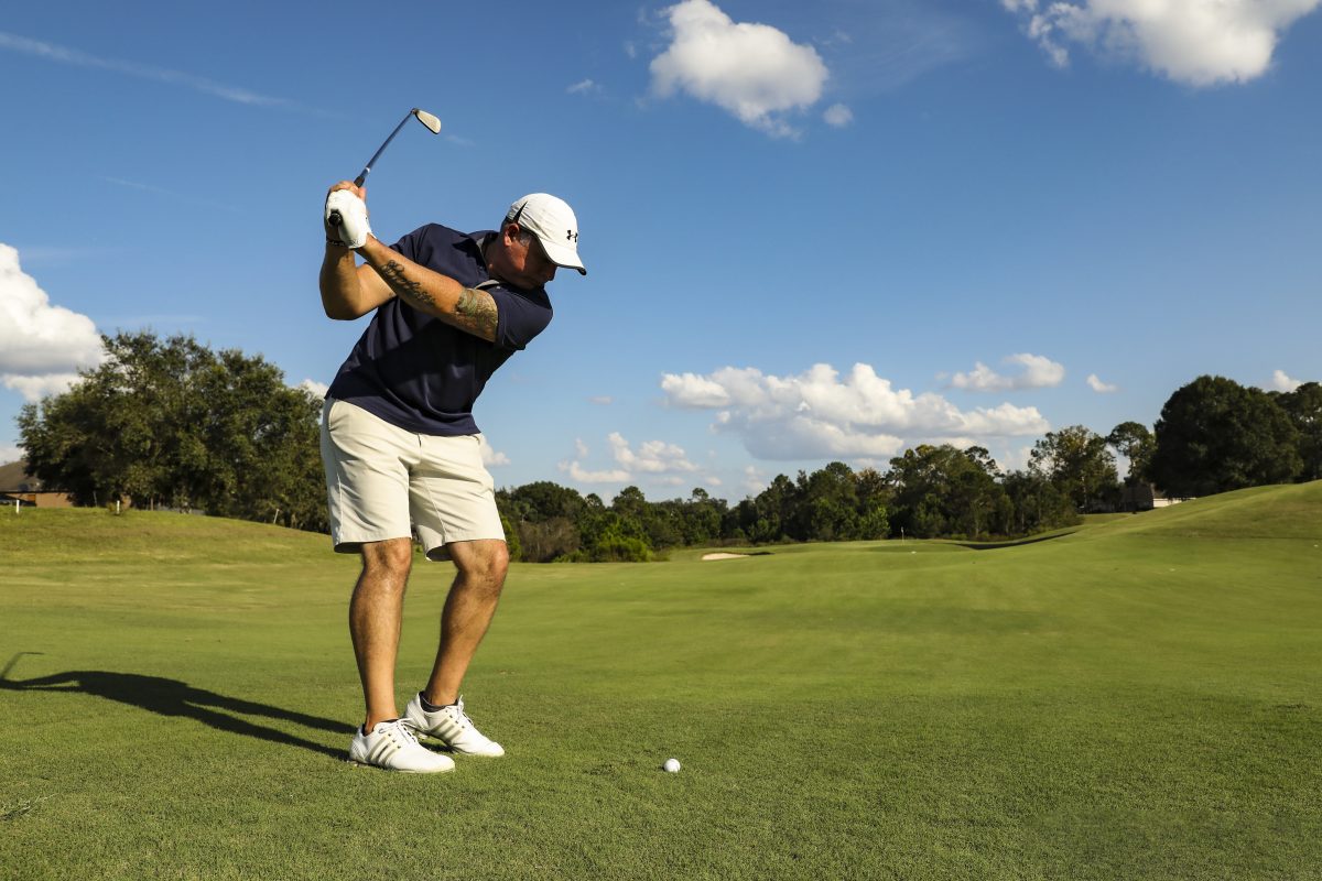 a man swinging golf club on sunny day