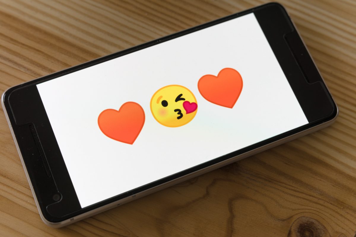 black ipad on brown wooden table showing hearts and kiss emoji