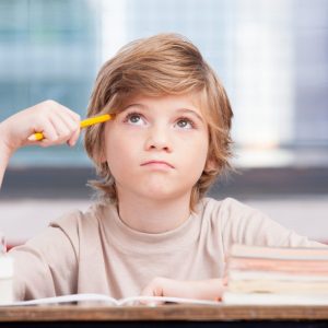 young boy sitting at a table thinking