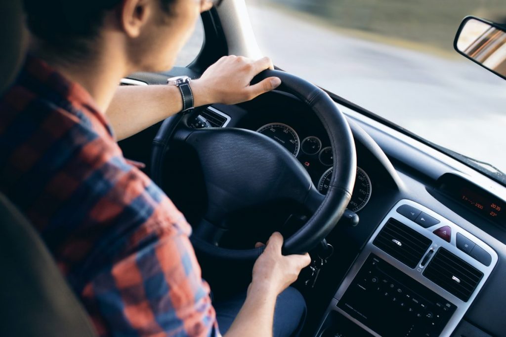 Man sitting inside vehicle with hands on steering wheel