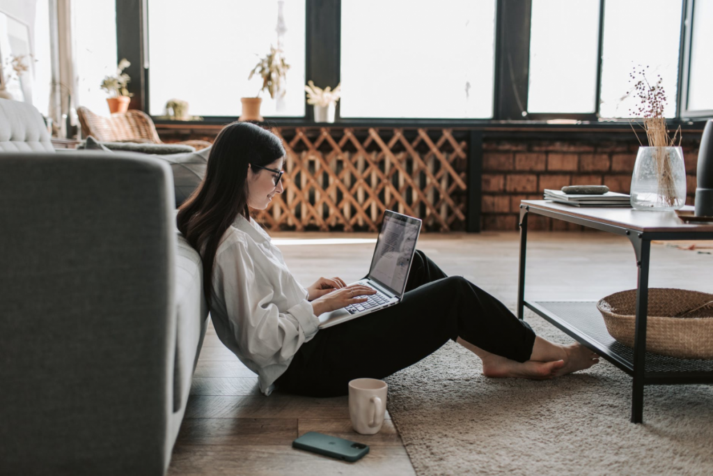 girl in a white sweater sitting on living room floor with computer in lap and coffee on floor
