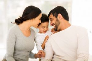 mom, dad, and son sitting together on a bed