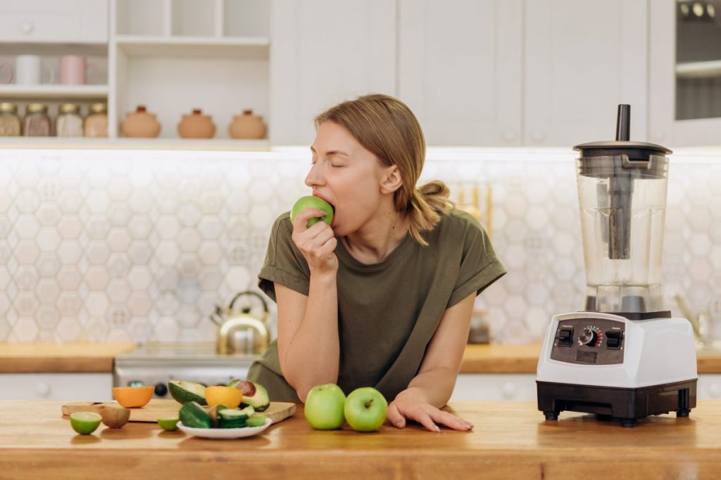 lady eating an apple at the counter with other fruit laying around
