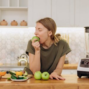 lady eating an apple at the counter with other fruit laying around