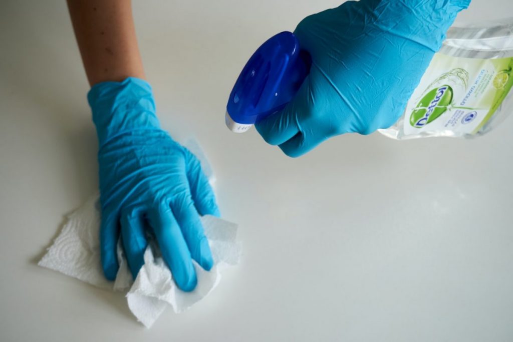 gloved hands with spray bottle and napkin cleaning surface