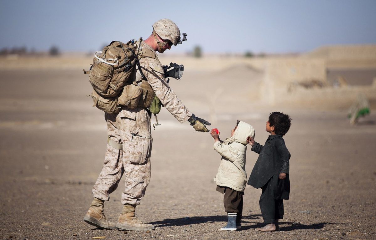 guy in us military uniform handing toy to small children