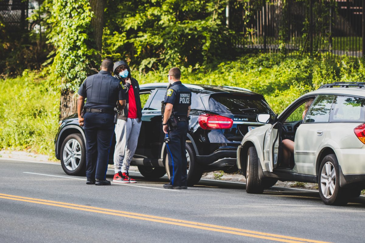 police men talking with young man in sweatpants standing beside black suv