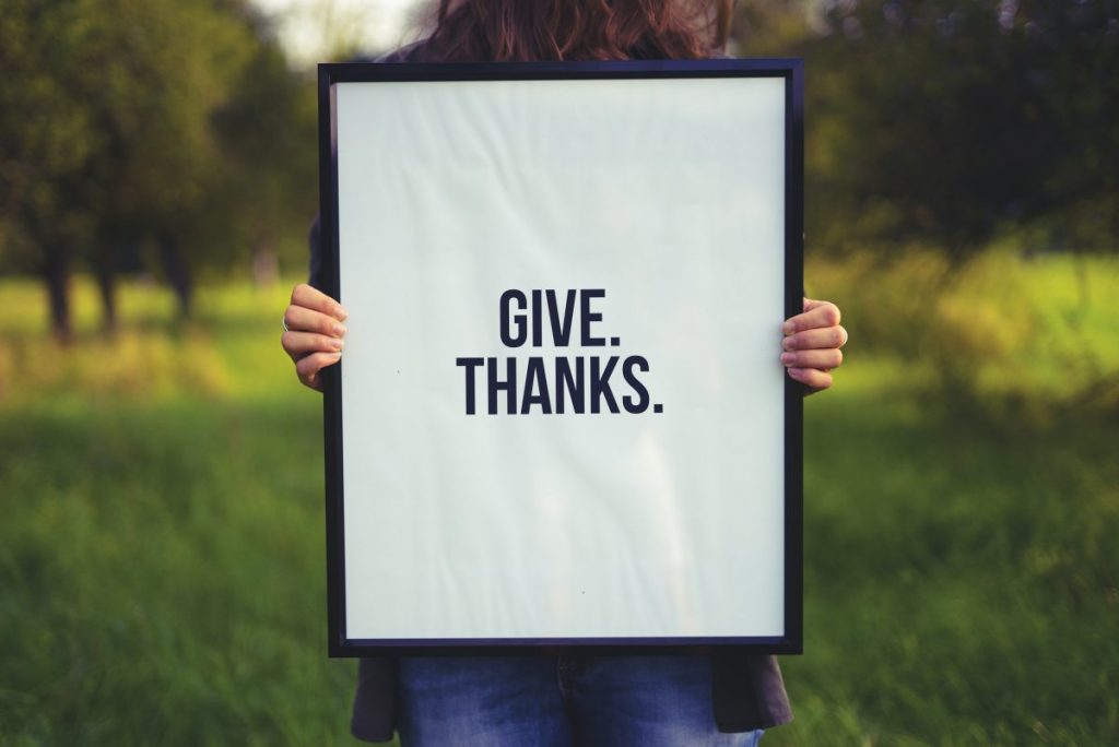 Woman holding a large framed poster that says give thanks
