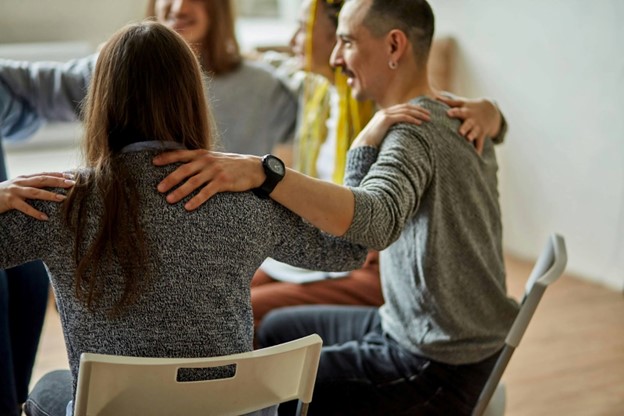 adults in therapy session with hands on shoulders in a circle