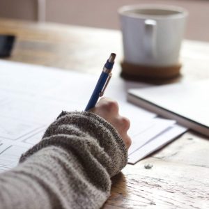 female hand with pen writing on a paper with coffee cup in background