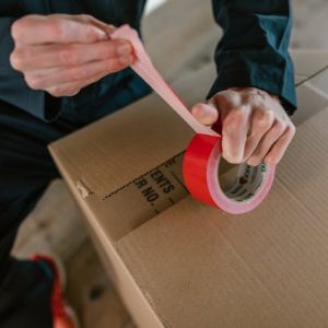 A man holding red tape above a moving box