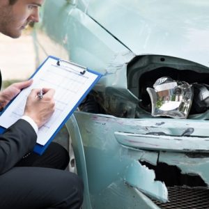 a person in a suite writing on a clipboard stooping next to a damaged car