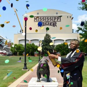 Mississippi State Graduate standing beside the MS Statue with confetti flying