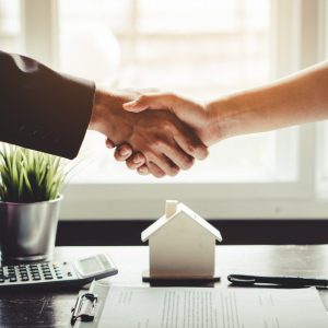 two people shaking hands over a table with a house and calculator and paperwork