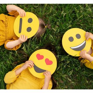 3 kids lying in the grass with emojis covering their face