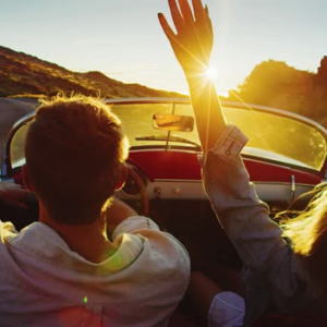 a couple driving a convertible car into the sunset