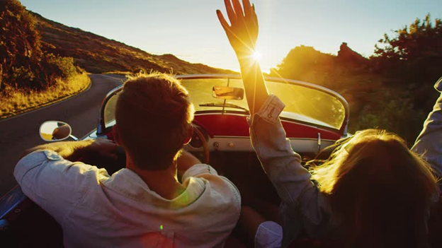a couple driving a convertible car into the sunset