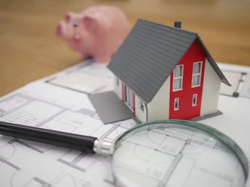 model home sitting on blueprints and magnifying glass