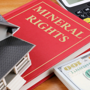 mineral rights law book sitting under a small house and stack of hundred dollar bills on a table