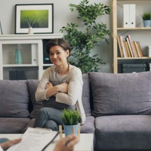 young woman sitting on a couch talking to therapist while holding pillow