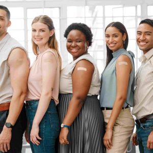 young adults standing behind one another all with a bandaid on their shoulders after getting a vaccine