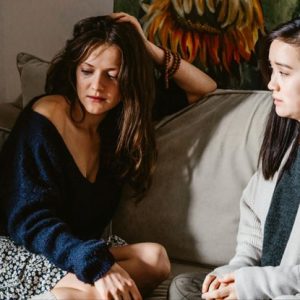 two ladies sitting on the couch. one being distraught