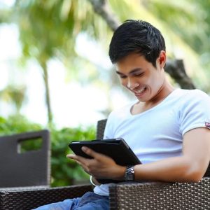 young man sitting in chair outside looking at tablet