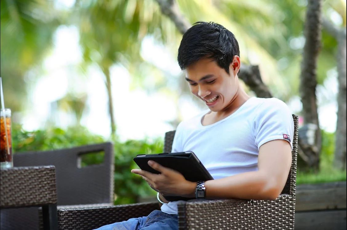 young man sitting in chair outside looking at tablet