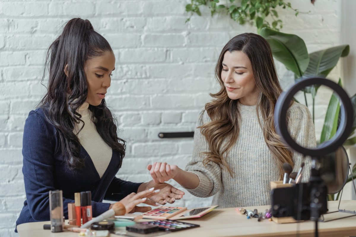 stylish young ladies recording a tutorial video while applying makeup while sitting at a table.