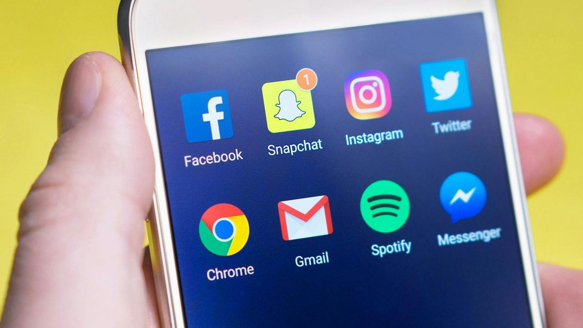 person holding iphone with social media icons on the screen