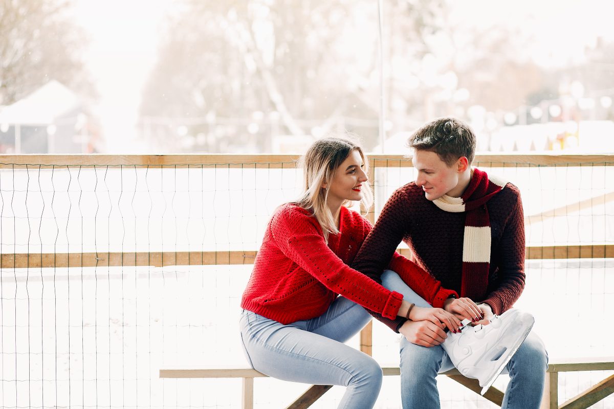 cute couple with red and black sweaters help each other skate