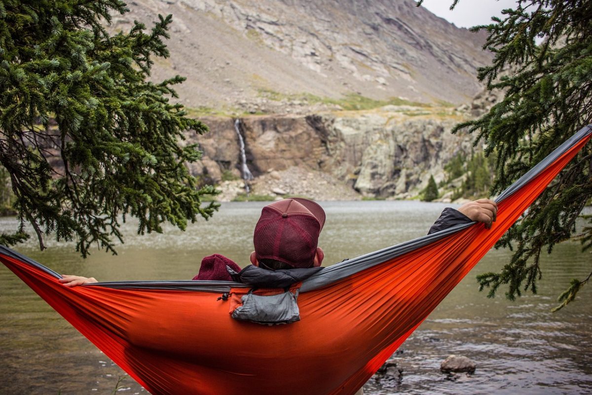 man sitting in red hammock looking over water at mountains