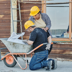two construction workers with yellow helmets working at wheelbarrow