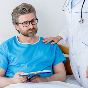 older gentleman sitting in the hospital bed with doctor touching his shoulder.