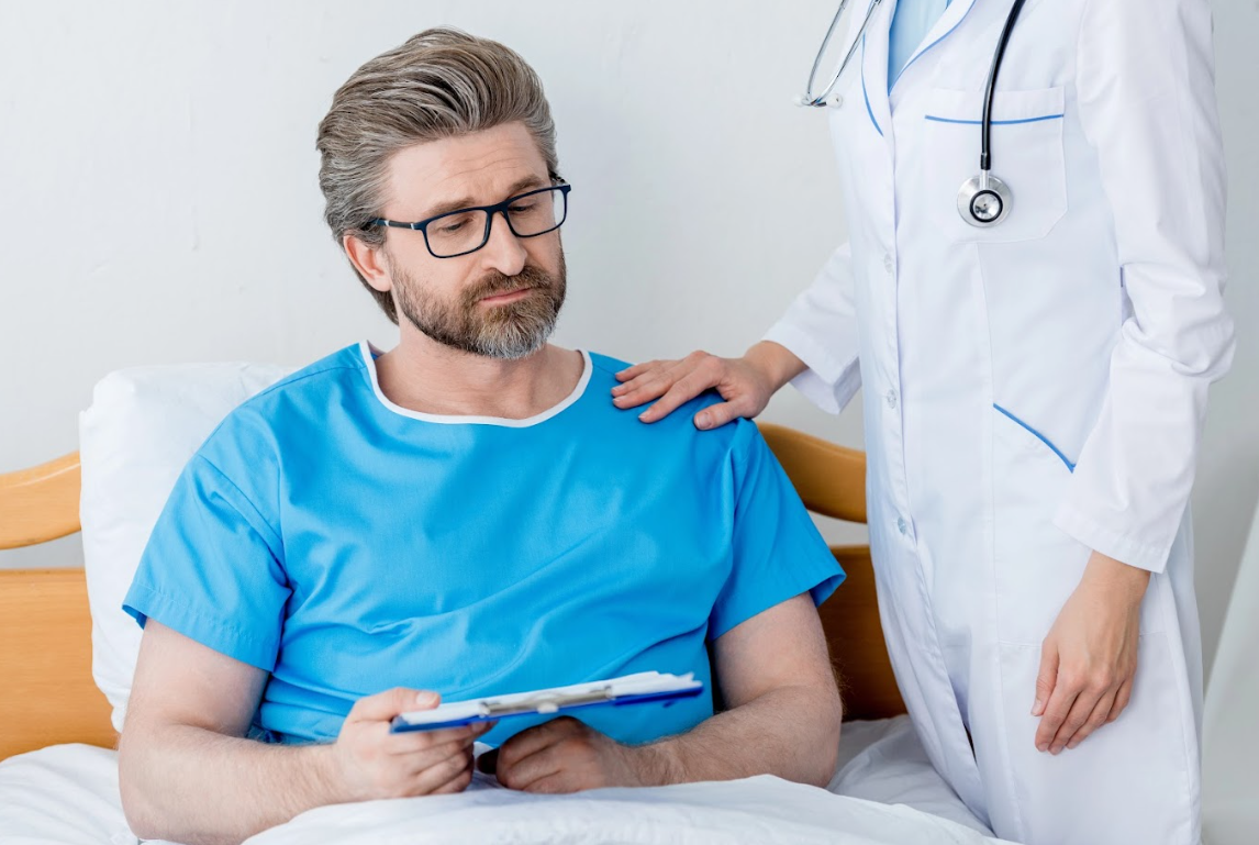 older gentleman sitting in the hospital bed with doctor touching his shoulder.