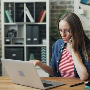 woman sitting at a table with computer and talking on the phone