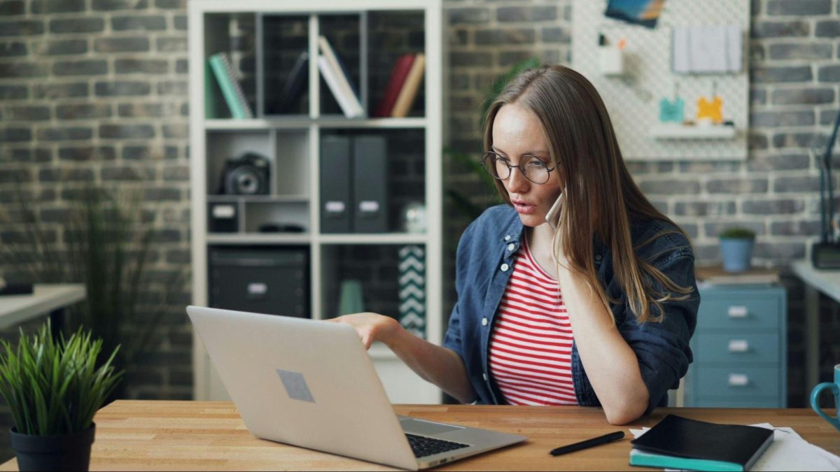 woman sitting at a table with computer and talking on the phone