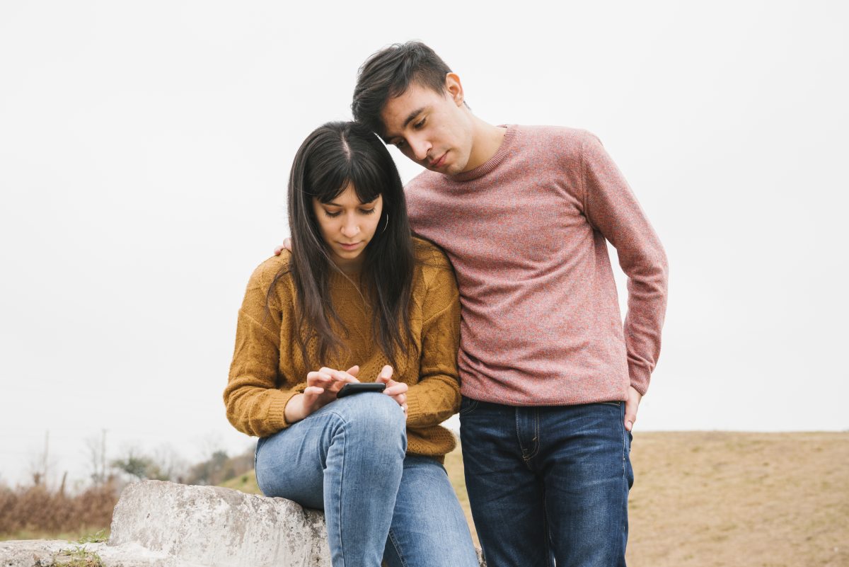 young couple looking at phone while sitting out in nature