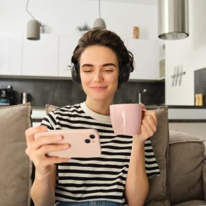 young woman watching videos on her smartphone while holding coffee in her other hand