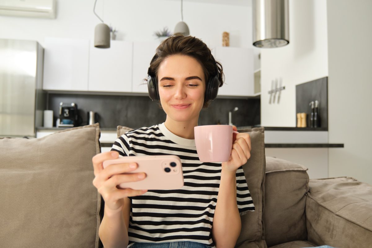 young woman watching videos on her smartphone while holding coffee in her other hand
