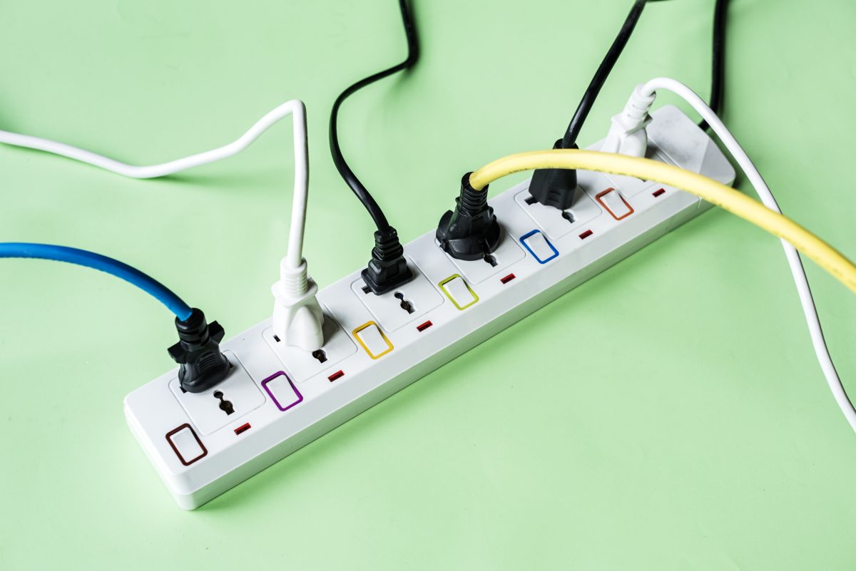 electrical power outlet with 6 plugs plugged in at one time sitting on green background