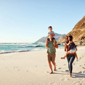 family of 4 walking on the beach with the kids in the arms of the parents