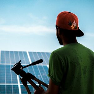 guy standing in front of solar panels holding a tripod for camera