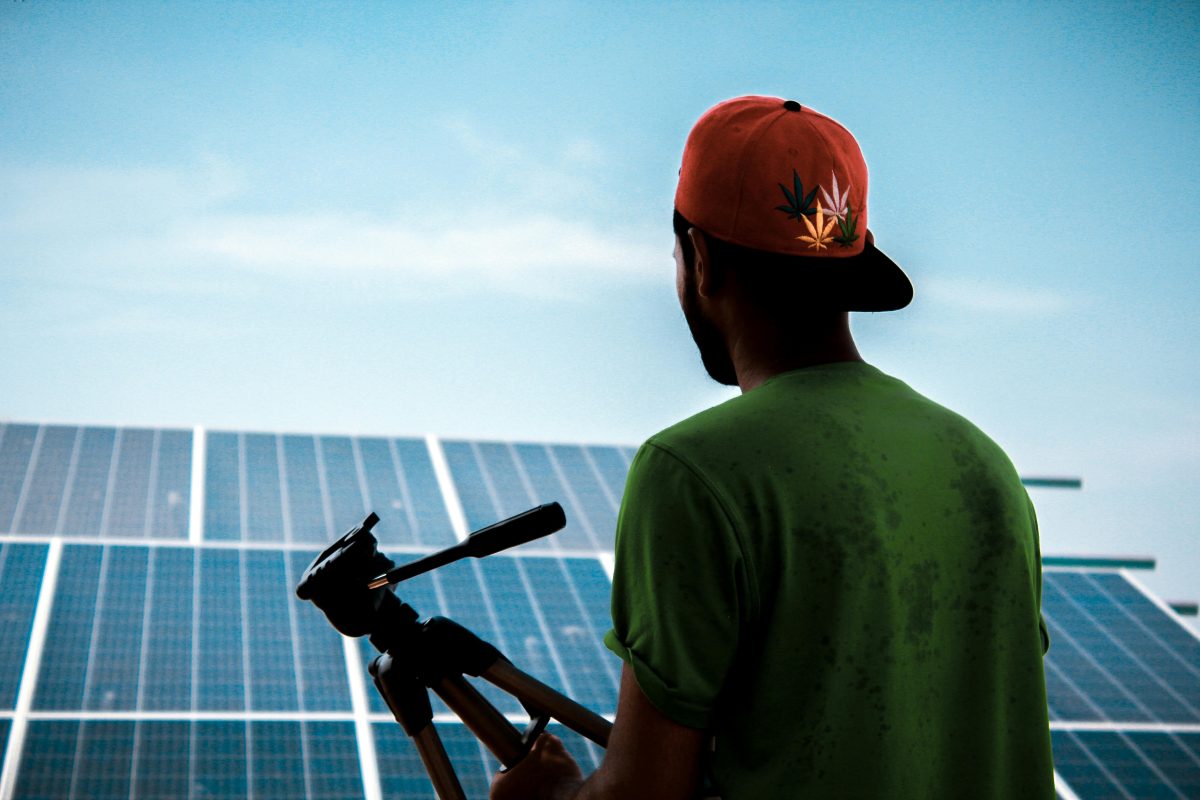 guy standing in front of solar panels holding a tripod for camera