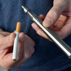 man holding a cigarette and a vape