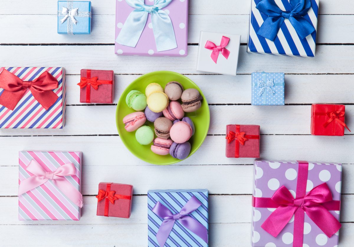 brightly colored gift boxes on a wooden table with a plate of macaroons
