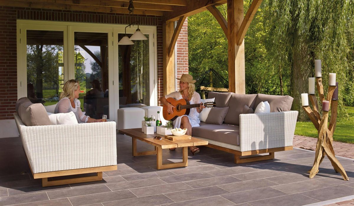 two women playing guitar while sitting on outdoor sofa couch