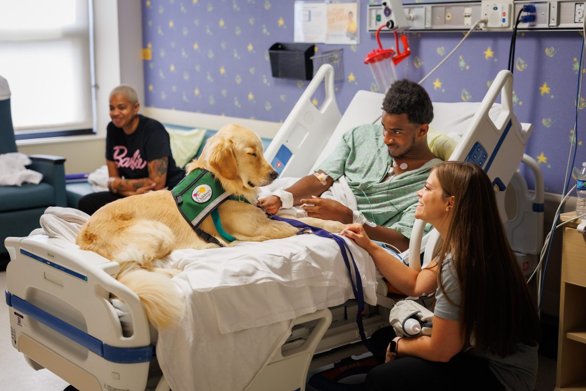 Children's of Mississippi patient Cayden Myers,15, of Camden gets a visit from Hollywood and the facility dog's handler, child life manager Cara Williams.