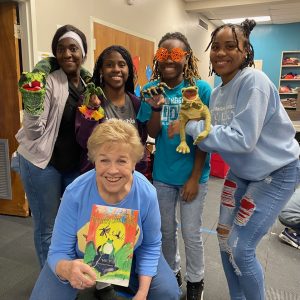 Diane Pleasant (kneeling center) presents The Creepy Creep Chorus as puppeteers (l to r) help tell the story: Naomi Elim, the snake puppet; Lakiyah Sutton, grasshopper; Mylah Sanders, spider; and Gabby Ward, frog.